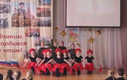На сцене дети в красных юбках и красных шляпках. На заднем плане баннер с надписью «Помним, гордимся и чтим!».