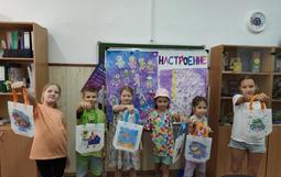 На изображении пятеро детей стоят в ряд, держа в руках сумки с рисунками. На заднем плане доска с надписью «НАСТРОЕНИЕ» и рисунками.
