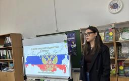 На фото — педагог, который рассказывает о Дне народного единства. На доске — поздравительный слайд ко Дню народного единства (4 ноября) с гербом РФ, картой России и надписями «Мы едины! Мы непобедимы!»
