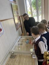 В комнате несколько детей в школьной форме рассматривают экспонаты в витринах.