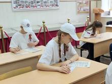 В классе три ученика в белых футболках и кепках. Они сидят за партами и пишут.