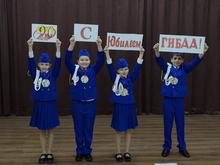 На изображении четверо детей в синих костюмах с белыми лентами. Они держат плакаты с надписями: «90 лет», «С юбилеем», «ГИБДД!»