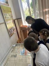 В комнате несколько детей в школьной форме рассматривают экспонаты в витринах.