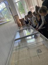 На изображении группа детей в школьной форме рассматривает витрину с газетами и экспонатами.