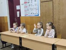 На изображении четыре девочки сидят за партой в классе. Одна из них подняла руку.
