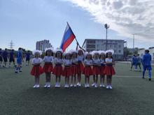 Танцевальный коллектив "От классического к современному танцу". Девочки в красных и белых костюмах с белыми бантами на головах держат флаг России.